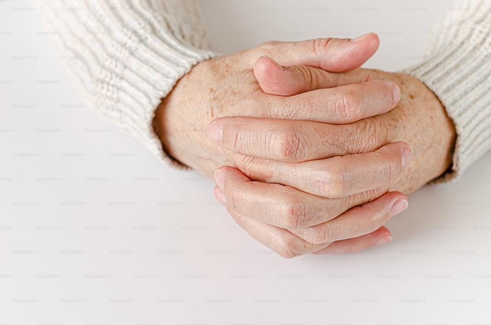 An elderly woman holding hand together on white background. Close up, copy space.
