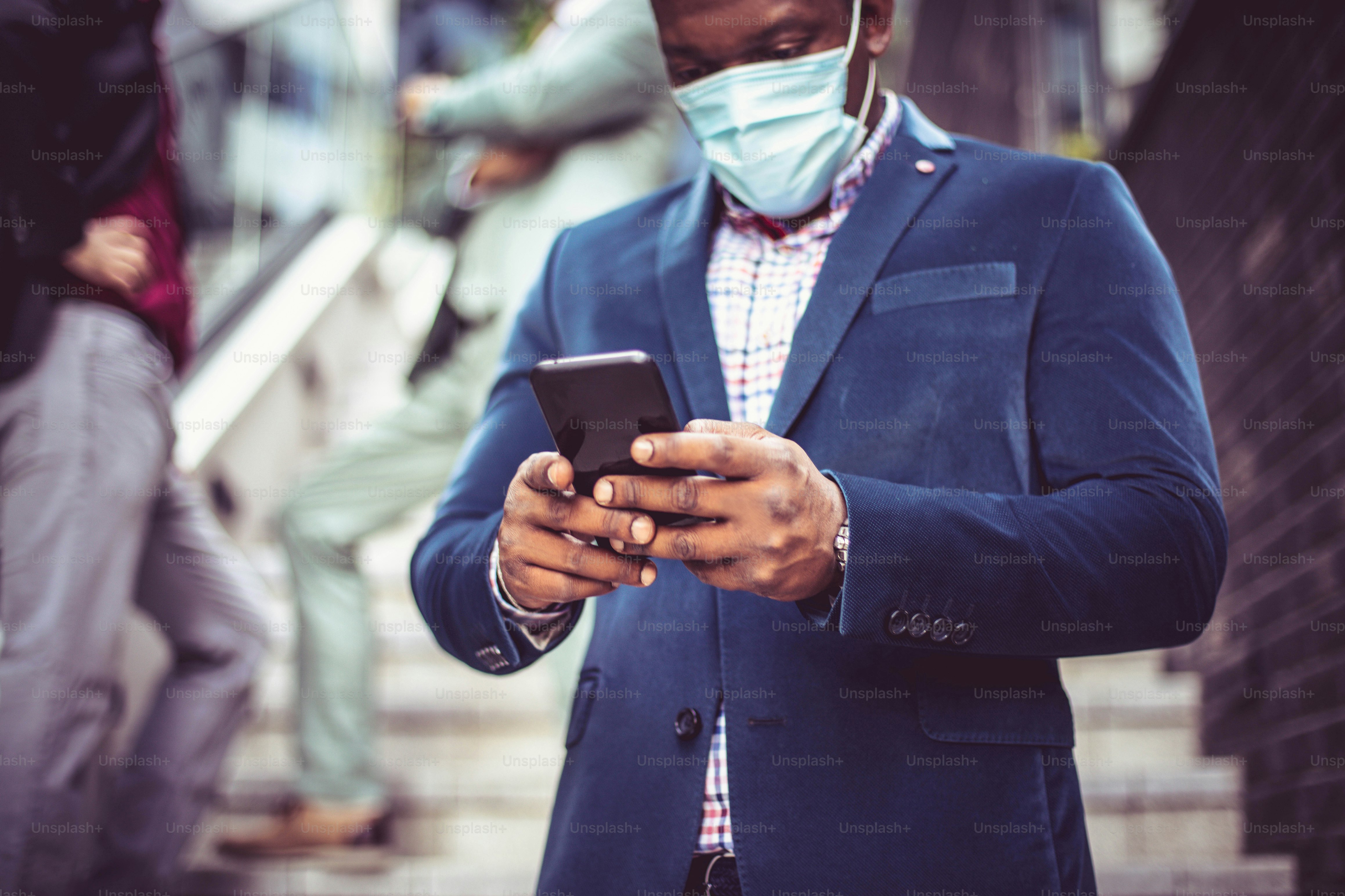 Three business men outside. African businessman typing on phone. Focus is on African man.