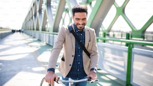 Ein junger Geschäftsmann pendelt mit dem Fahrrad zur Arbeit im Freien in der Stadt, zu Fuß auf einer Brücke.
