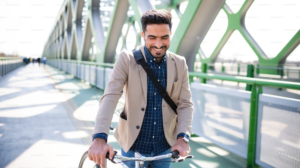 Un giovane pendolare dell'uomo d'affari con la bicicletta che va a lavorare all'aperto in città, camminando sul ponte.