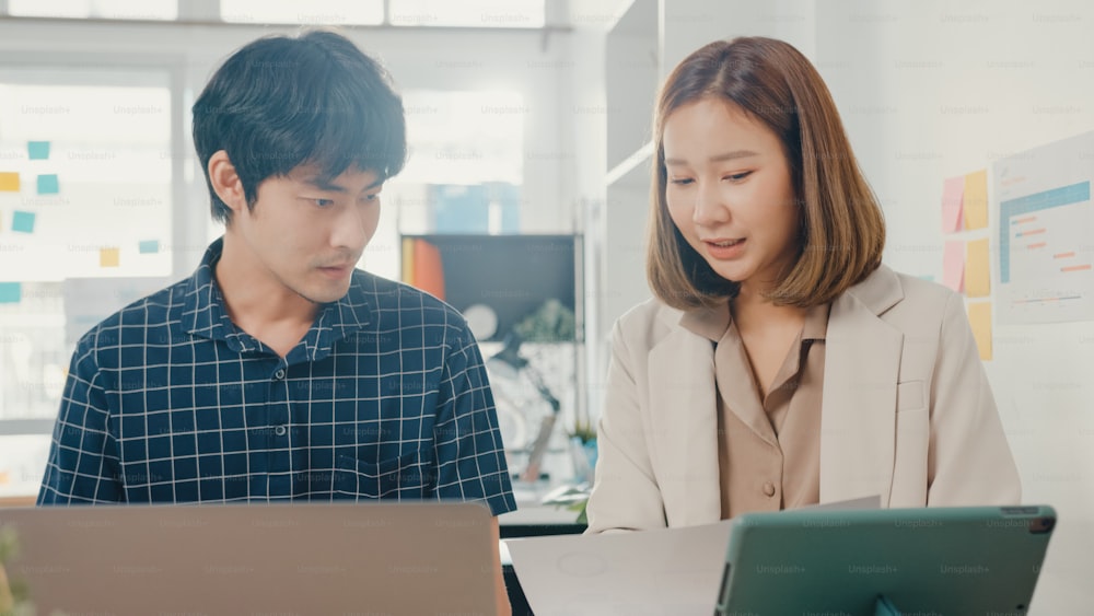 Young coworker asia creative businessman and businesswoman manager discuss project compare point in paperwork and laptop on table working and communicate together sitting on office desk at workplace.