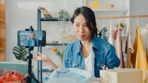 Junge asiatische Modedesignerin mit Handy Empfang Bestellung und zeigt Kleidung Aufnahme Video Live-Streaming online im Geschäft. Kleinunternehmer, Online-Markt-Lieferkonzept.