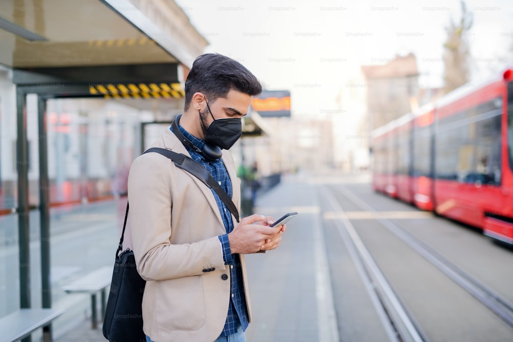 Un joven hombre de negocios que viaja diariamente con un teléfono inteligente de camino al trabajo al aire libre en la ciudad, concepto de coronavirus.