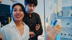 Asia businesspeople stand behind transparent glass wall listen manager pointing progress work and brainstorm meeting and worker post sticky note on wall. Business inspiration, Share business ideas.
