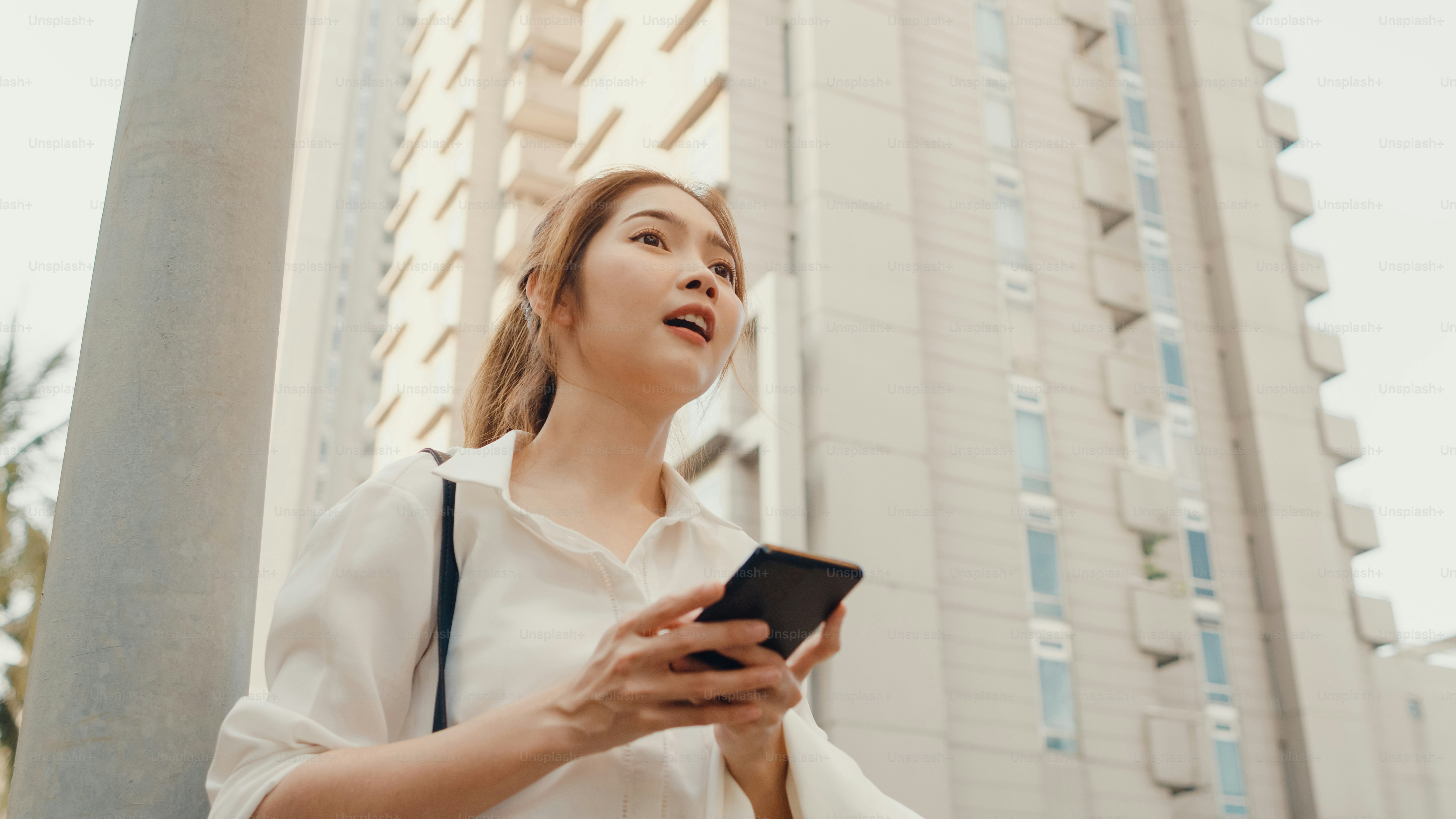 A woman in a white shirt holding a smartphone outdoors near a tall building