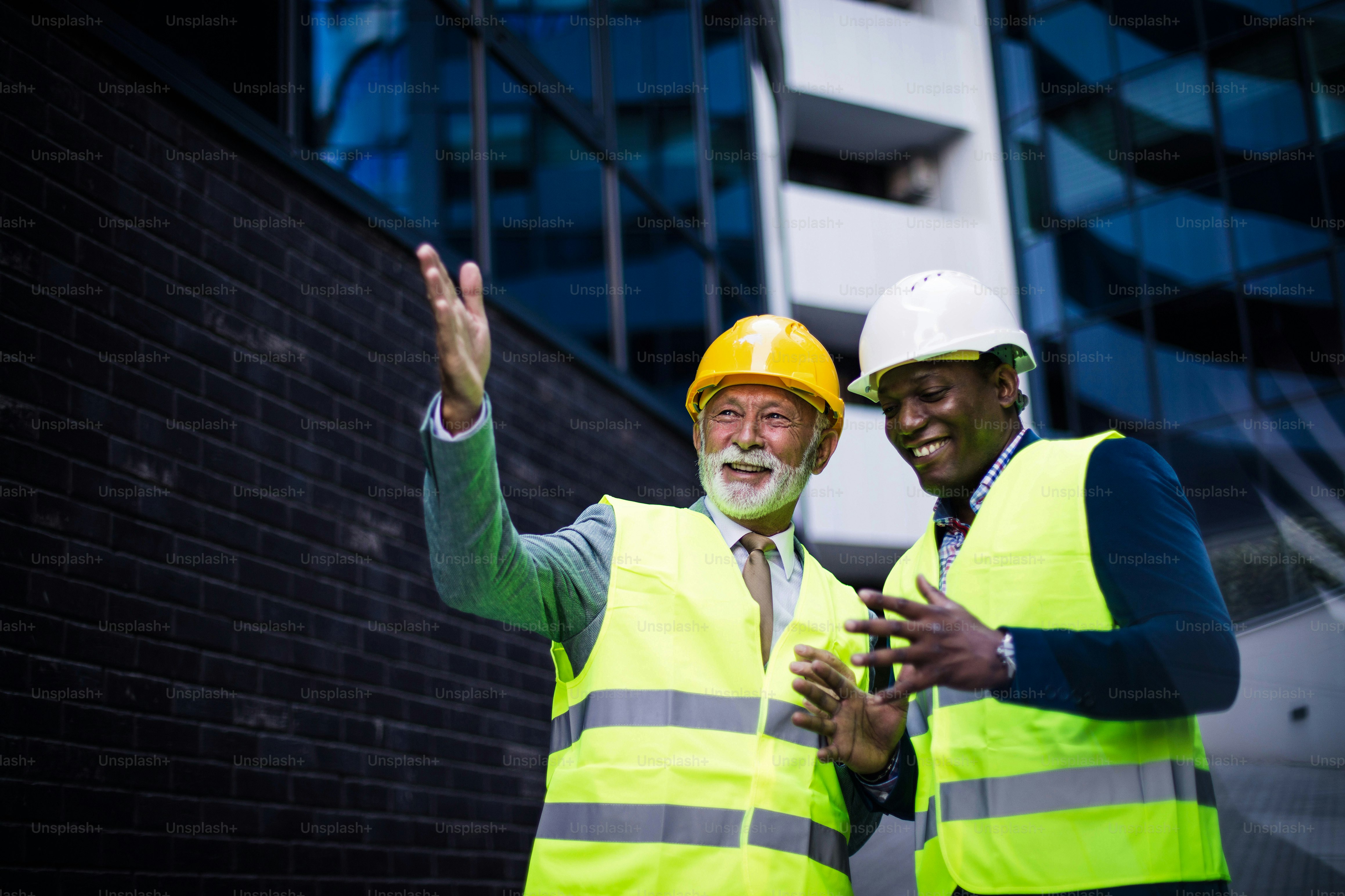 Mature engineer discussing the structure of the building with architects colleague at construction site. Businessmen talking