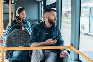 Young handsome man riding a bus while using a smartphone and looking through the window