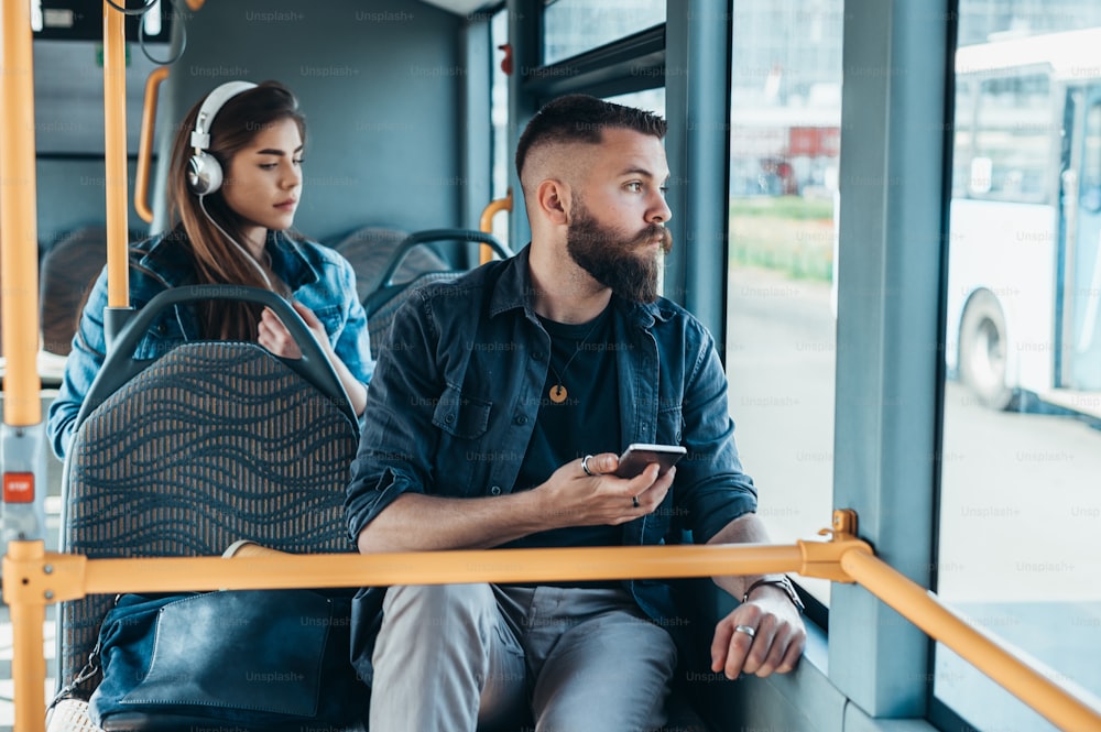 Young handsome man riding a bus while using a smartphone and looking through the window