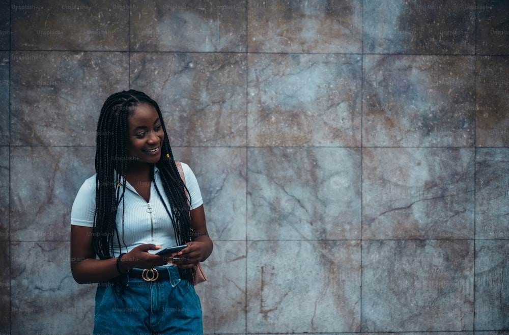 Donna afroamericana allegra che usa lo smartphone mentre è fuori in una città durante un giorno
