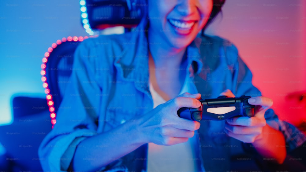 Heureux asiatique fille gamer porter casque et joystick contrôleur parler avec un ami se sentir amusant et excité avec la compétition jeu en ligne dans le studio à domicile du salon néon la nuit, activité de quarantaine à domicile.