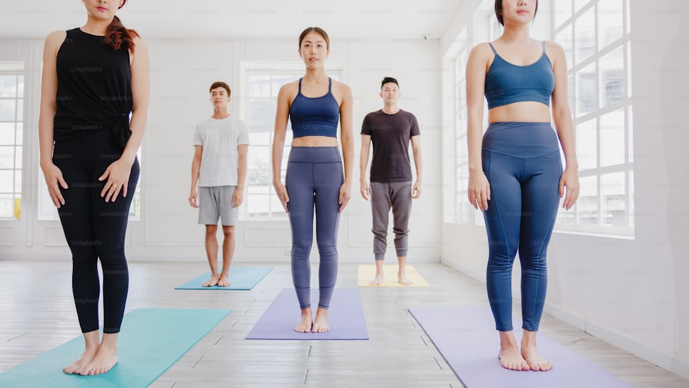 Young Asian sporty attractive people practicing yoga lesson with instructor. Asia group of women exercising healthy lifestyle in fitness studio. Sport activity, gymnastics or ballet dancing class.