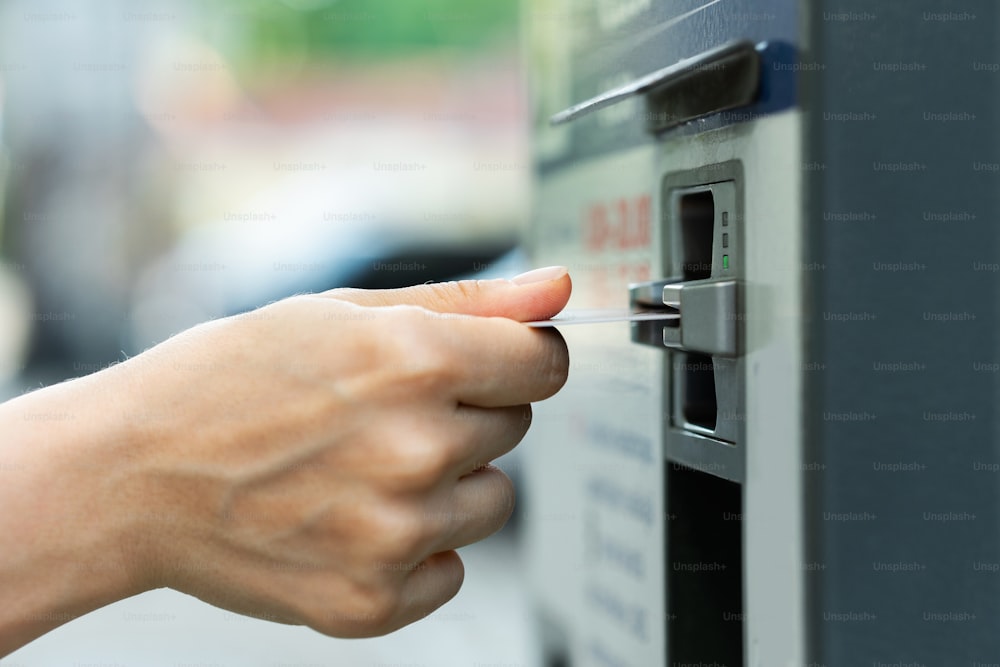Gros plan d’une main féminine avec une carte de crédit et un distributeur automatique de billets