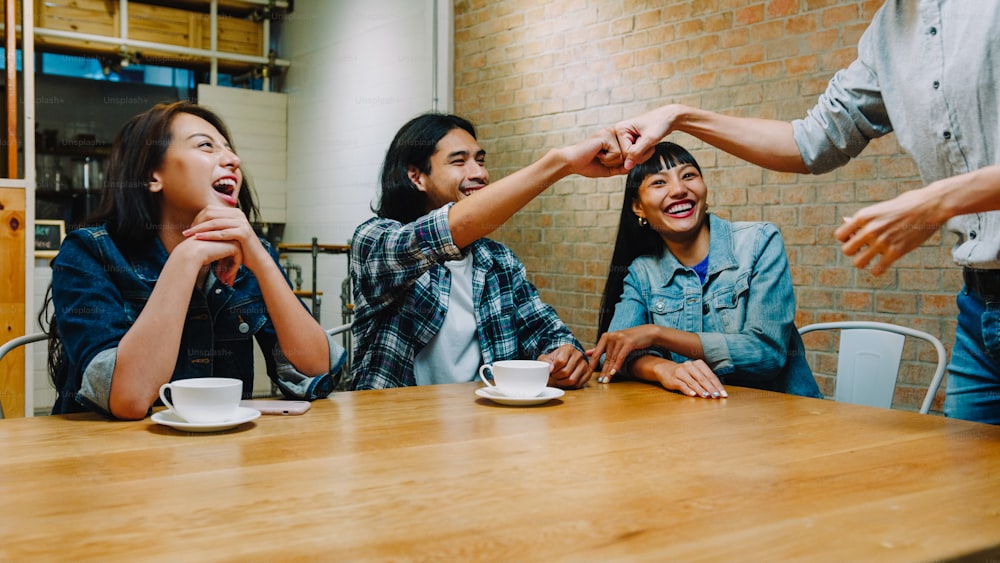 Group of happy young Asia friends having fun a great time and greeting with friendship fist pump while sitting together at cafe restaurant. Coffee shop holiday activity, friendship lifestyle concept.