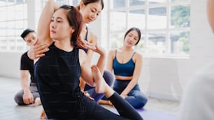 Young Asian sporty attractive people practicing yoga lesson with instructor. Asia group of women exercising healthy lifestyle in fitness studio. Sport activity, gymnastics or ballet dancing class.