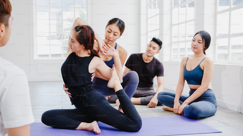 Young Asian sporty attractive people practicing yoga lesson with instructor. Asia group of women exercising healthy lifestyle in fitness studio. Sport activity, gymnastics or ballet dancing class.