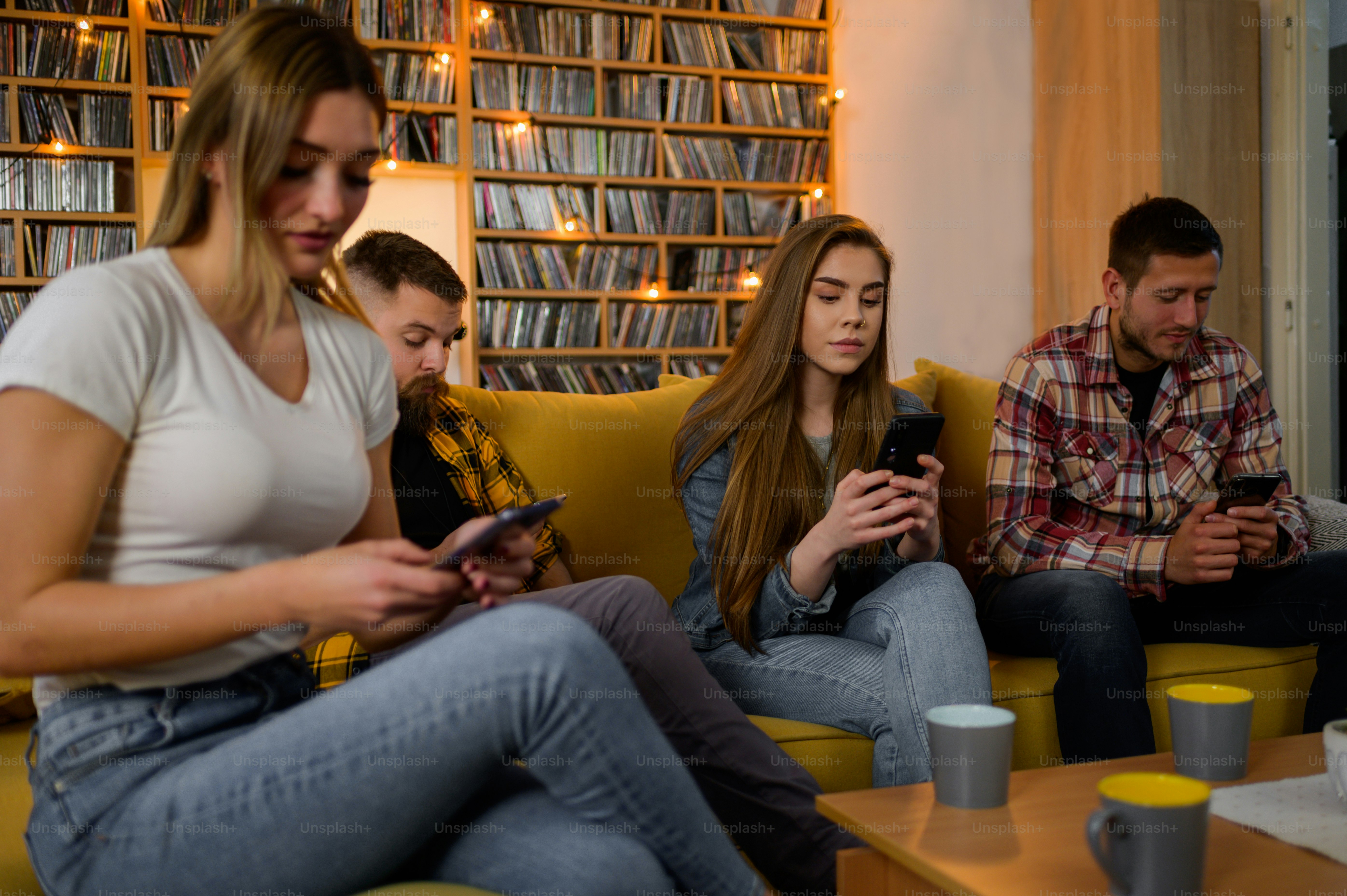 Sekelompok teman nongkrong di pesta rumah sambil menggunakan smartphone dan mengabaikan satu sama lain