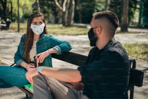 코로나 바이러스 전염병으로 인해 보호 마스크를 쓰고 캠퍼스의 벤치에 앉아 거리를 두는 두 명의 어린 학생