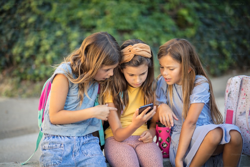 흥미로운 비디오를 볼 시간입니다.  세 명의 어린 소녀들이 함께 스마트폰을 사용하고 있다.