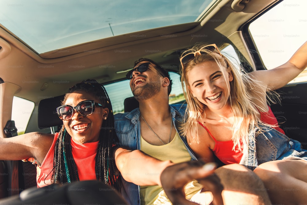 Three best friends enjoying traveling in the car, sitting in rear seat and having lots of fun on a road trip.