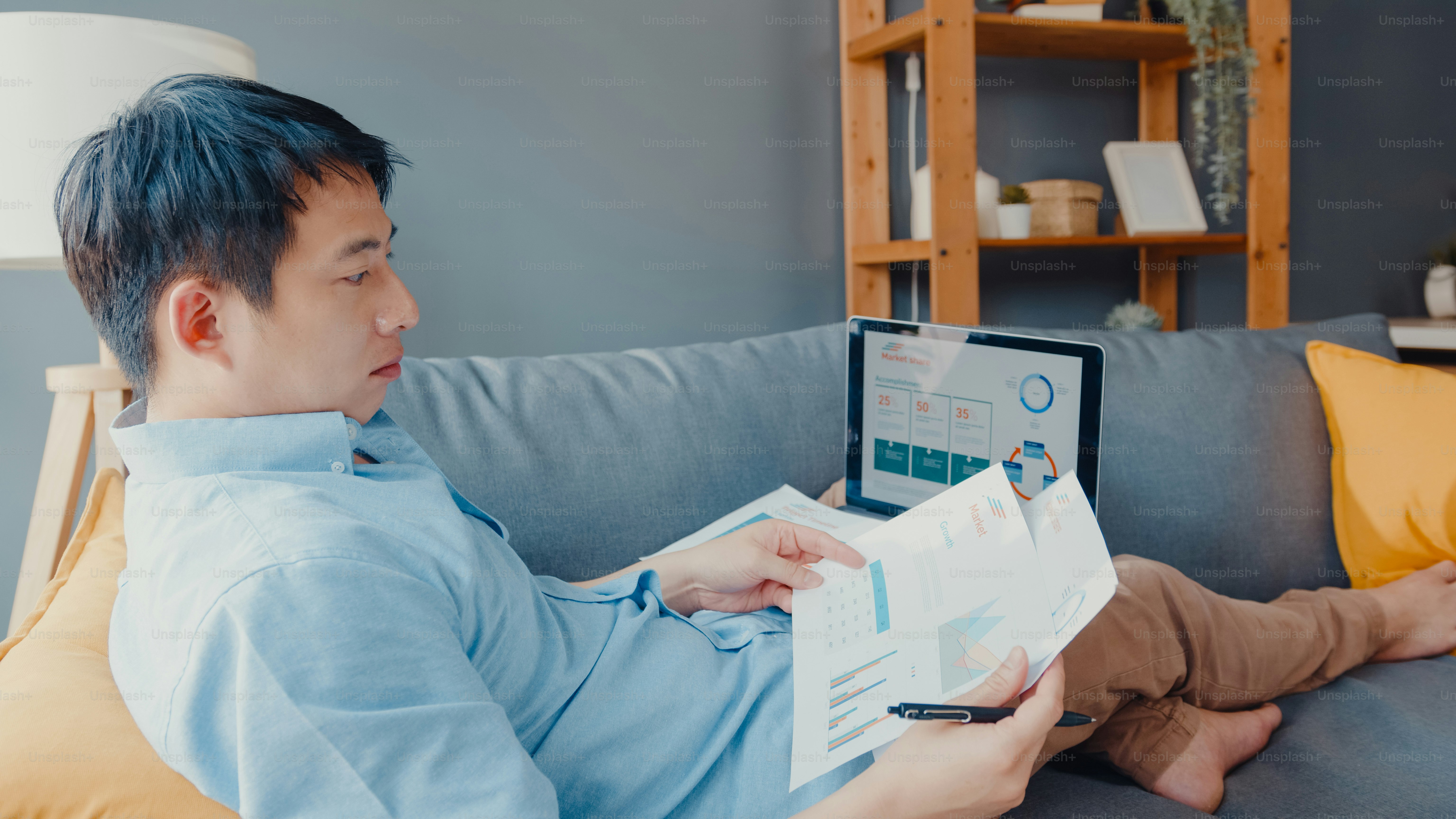 Freelance Asia guy casual wear using laptop online learning in living room at house. Working from home, remotely work, distance education, social distancing, quarantine for corona virus prevention.