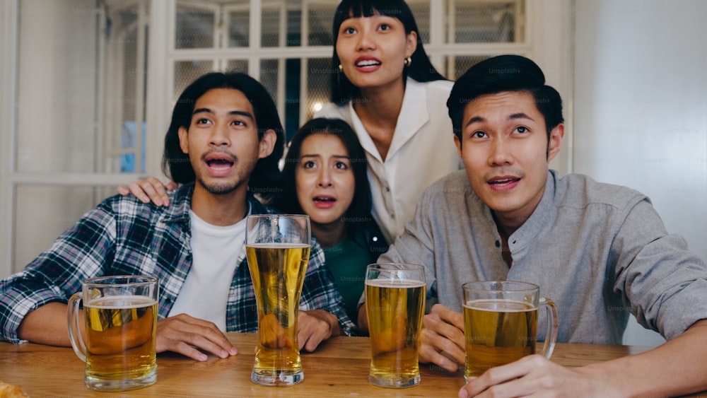 Grupo de jóvenes turistas asiáticos amigos que ven fútbol en deportes TV, beben cerveza con alcohol y tienen una fiesta de reunión en el club nocturno en Khao San Road. Los mochileros viajeros viajan a Bangkok, Tailandia.