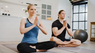 Young American couple in sportswear doing yoga exercise working out in kitchen at home at morning. Sport and recreation activity, social distancing, quarantine for corona virus prevention concept.