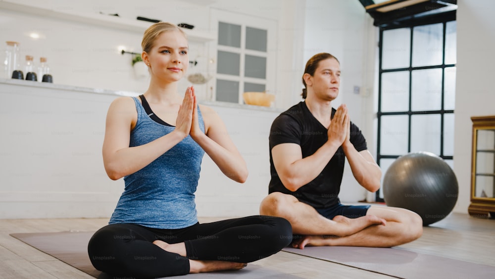 Young American couple in sportswear doing yoga exercise working out in kitchen at home at morning. Sport and recreation activity, social distancing, quarantine for corona virus prevention concept.