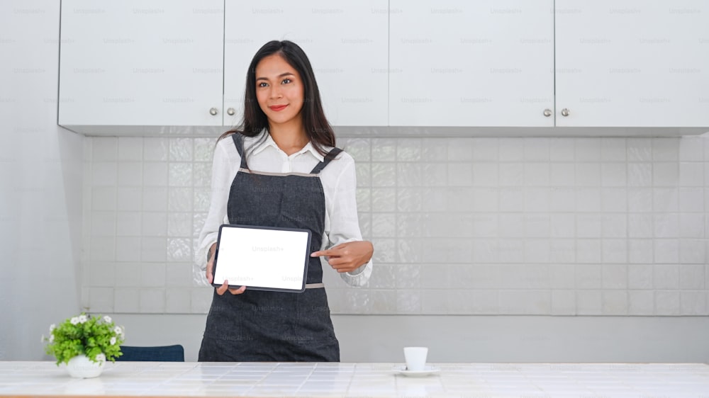 Attractive female business owner in apron showing digital tablet.