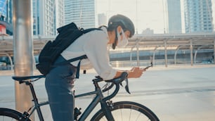 Asian businesswoman carry backpack wear anti virus protection mask take bicycle walk and check phone in city street go to work at office. commute to work, Business commuter for covid-19 concept.