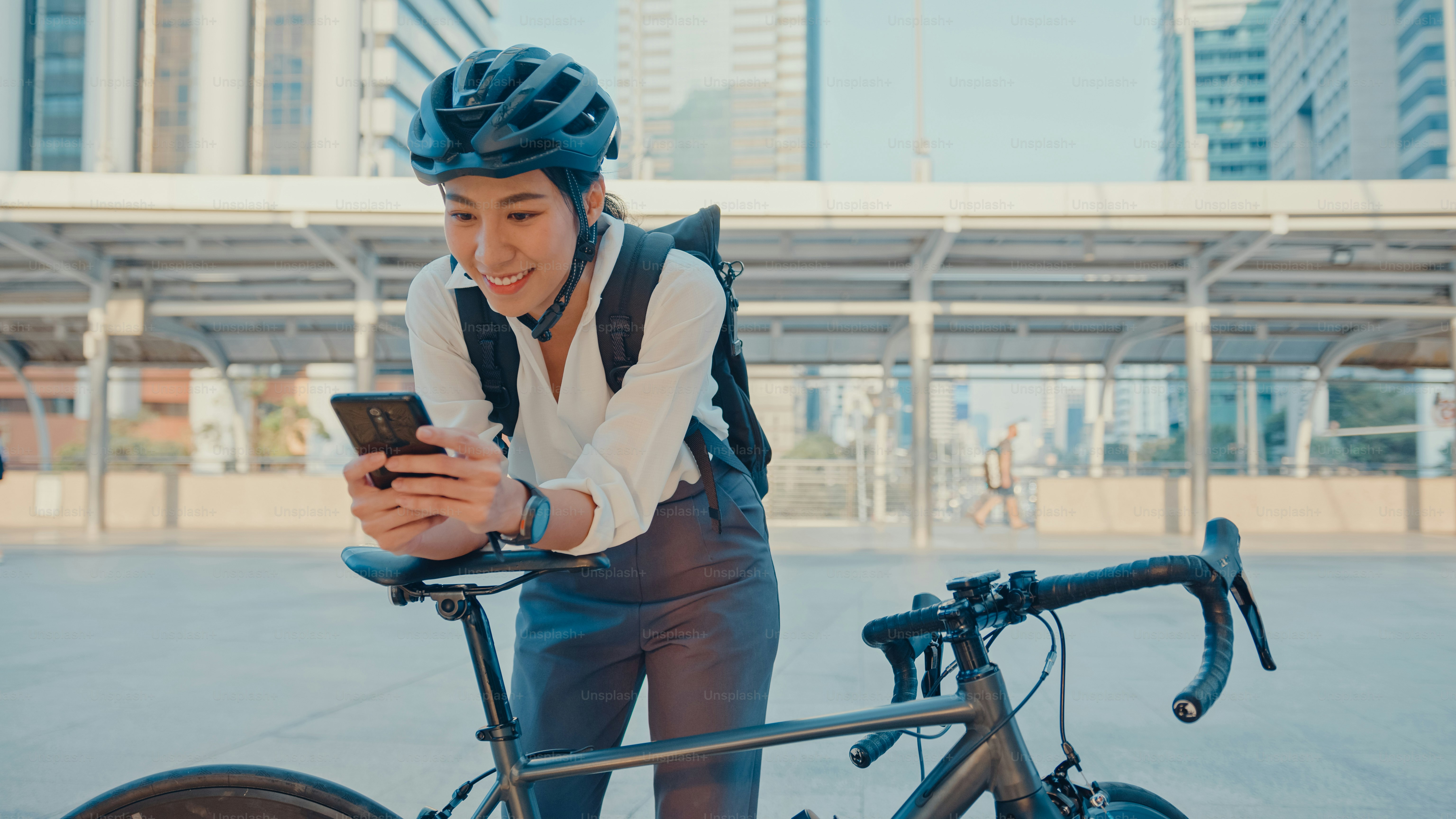 Sorria empresária asiática com mochila usar telefone inteligente olhar câmera na cidade stand na rua com bicicleta ir para o trabalho no escritório. Menina do esporte usar o telefone para o trabalho. Deslocamento para o trabalho, Deslocamento de negócios na cidade.