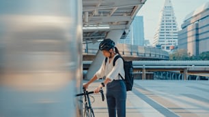Femme d’affaires asiatique aller au travail au bureau, marcher et sourire, porter un sac à dos, regarder autour de soi, prendre du vélo dans la rue, autour d’un bâtiment, dans une rue de la ville. Vélo, Trajet domicile-travail à vélo, Concept de navette d’affaires.