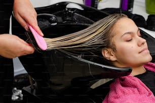 Peluquero aplicando mascarilla capilar y peinando el cabello mojado de los clientes con un cepillo en un fregadero negro.