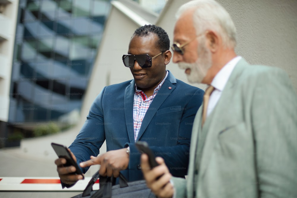 Two business men outdoors. Using smart phones.