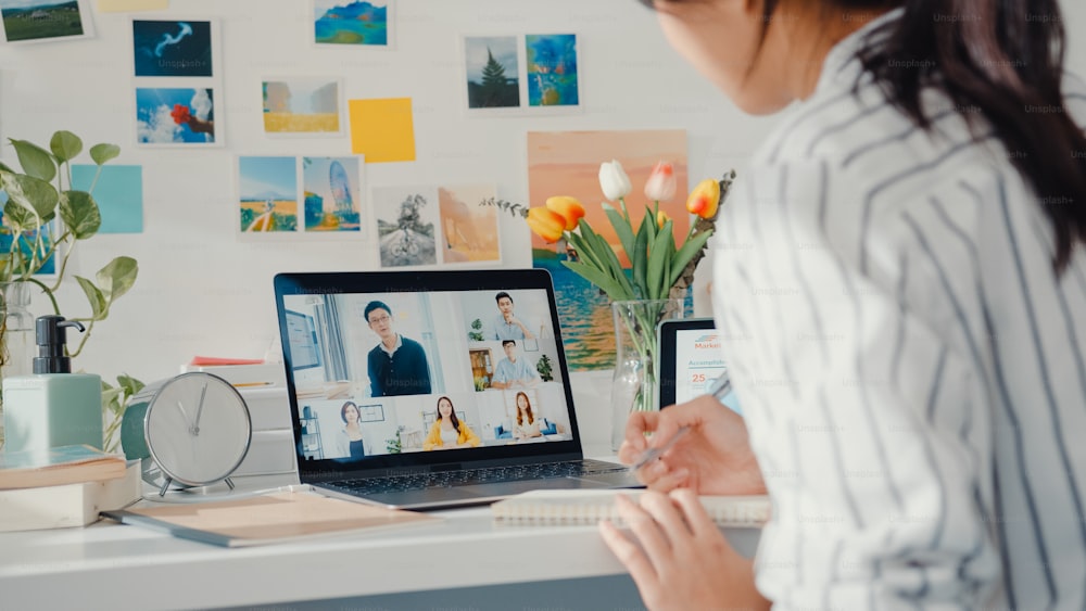 Young asia female employee listen leader on video call with diverse multiracial colleagues on online with laptop at home. Distance learning. Girl student learn online at house, Online meeting concept.