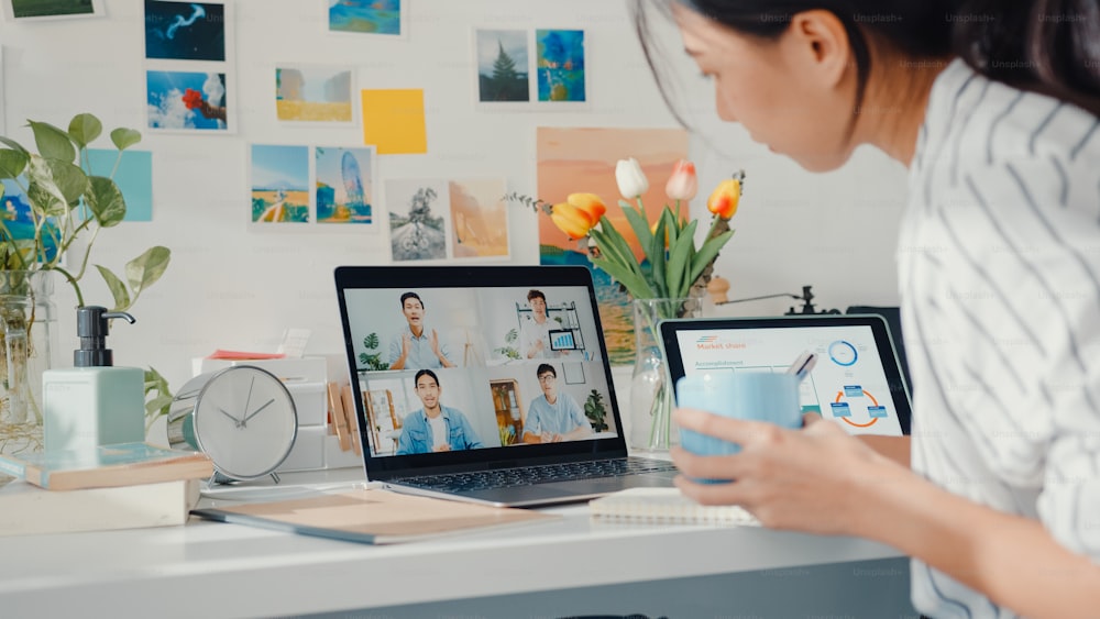 Jeune employée asiatique écouter leader lors d’un appel vidéo avec divers collègues multiraciaux en ligne avec un ordinateur portable à la maison. Enseignement à distance. Une étudiante apprend en ligne à la maison, concept de réunion en ligne.