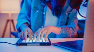 Primer plano feliz chica asiática dj uso launchpad sintetizador teclado mezclador de sonido usar auriculares hizo música en computadora portátil en línea en vivo en la sala de estar estudio en casa por la noche. Concepto de creador de contenido.