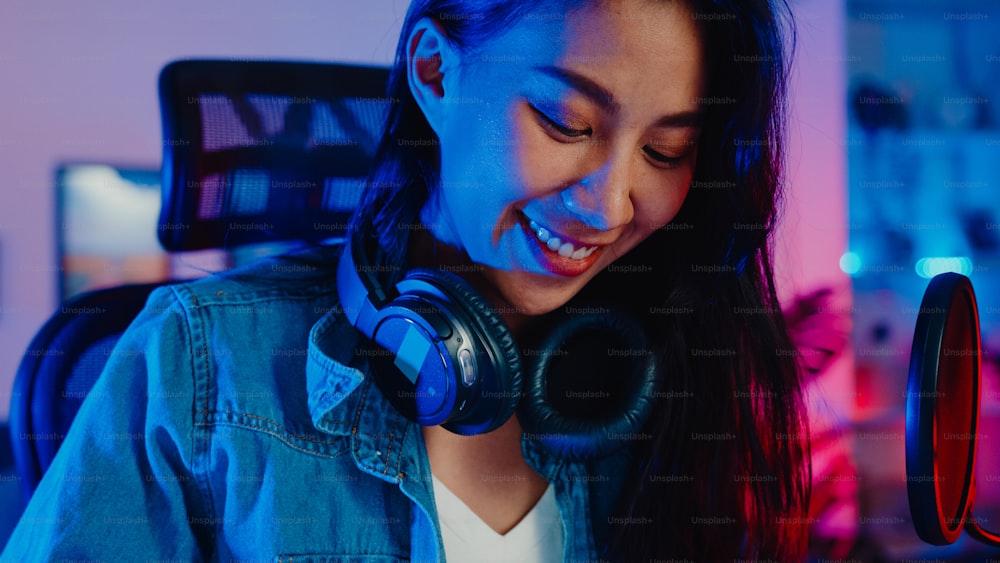 Happy asia girl blogger play synthesizer keyboard wear headphone and record music with sound mixer on laptop in living room home studio at night. Music content creator, tutorial, Broadcast concept.