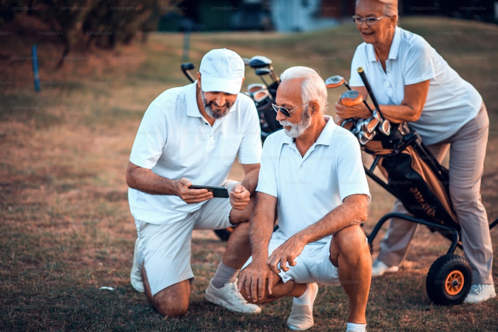 Golfistas senior en pista. Dos hombres usando un teléfono inteligente.