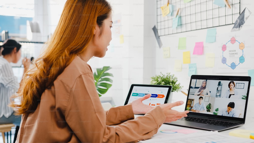 Asia businesspeople using laptop talk to colleagues discussing business brainstorm about plan in video call meeting in new normal office. Lifestyle social distancing and work after corona virus.