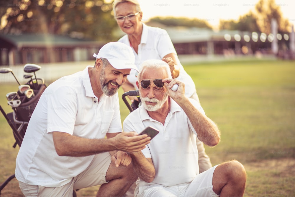 Golfistas senior en pista. Dos hombres usando un teléfono inteligente.