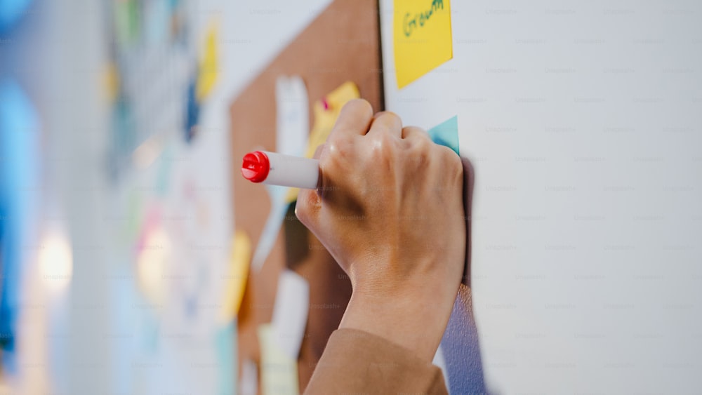 Group of young Asia businesspeople discussing business brainstorming meeting working together sharing data and writing whiteboard on wall with sticky note in night office. Coworker teamwork concept.