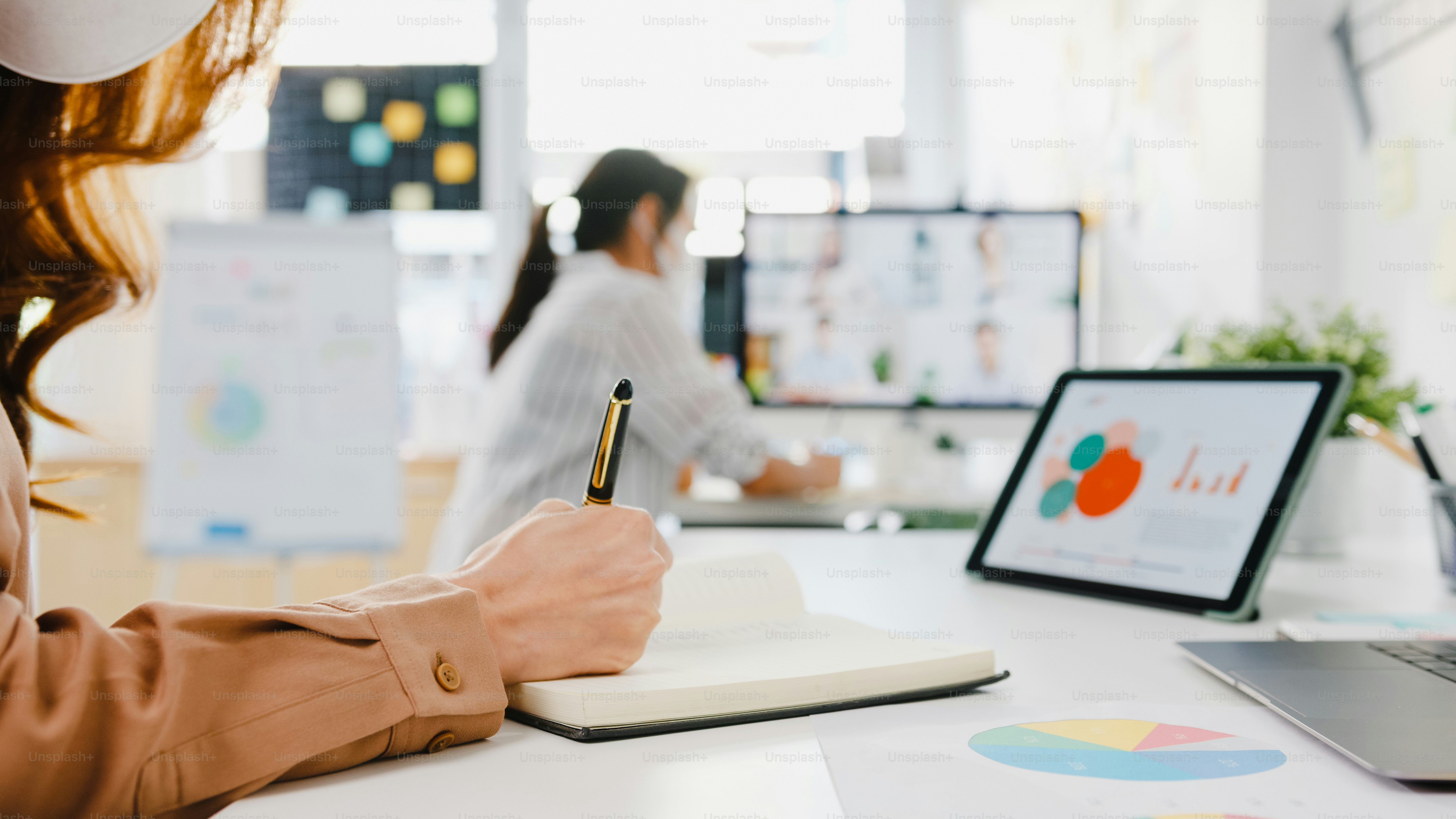 Asia businesspeople wear face mask using desktop talk to colleagues discussing brainstorm about plan in video call meeting in new normal office. Lifestyle social distancing and work after coronavirus.