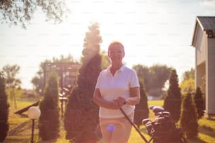 Smiling senior golfer woman standing outdoors and looking at camera.