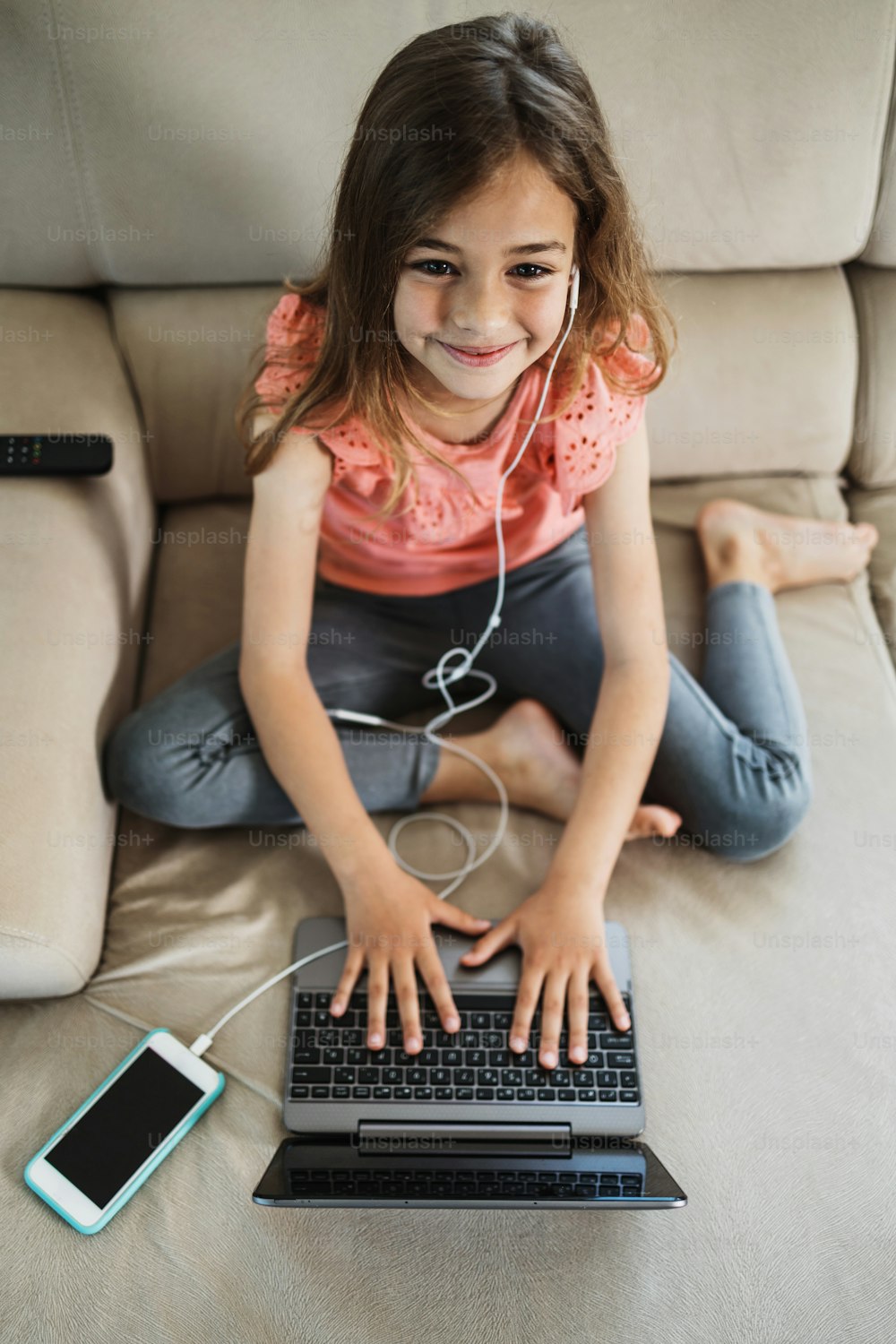 Menina bonita deita-se no sofá da sala de estar e usa um laptop para surfar, aprender e comunicação. Ela está feliz e sorriu.