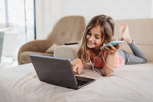 La hermosa chica se acuesta en el sofá de la sala de estar y usa una computadora portátil para navegar, aprender y comunicarse. Ella está feliz y sonríe.