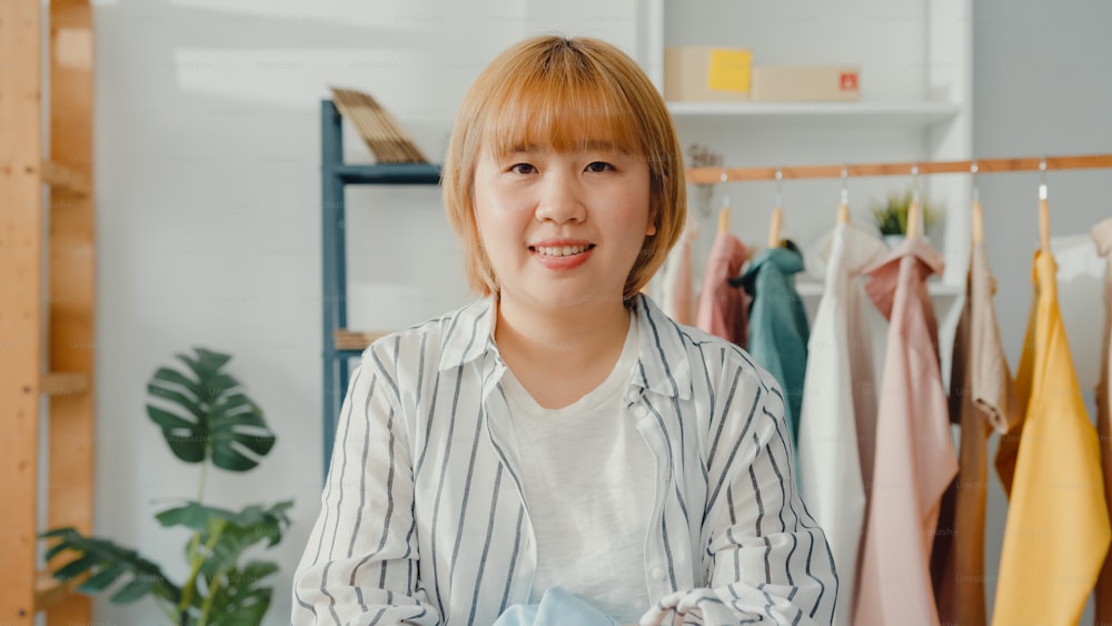 Porträt der jungen Asia-Modedesignerin, die sich glücklich lächelt, die Arme verschränkt und in die Kamera schaut, während sie im Heimbüro arbeitet. Kleinunternehmer, Online-Markt-Lieferkonzept.