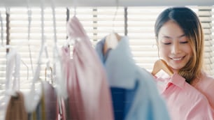 Belle jeune femme asiatique attrayante choisissant ses vêtements de tenue de mode dans le placard à la maison ou au magasin. Fille penser à quoi porter chemise décontractée. Vestiaire de la garde-robe ou du magasin de vêtements.