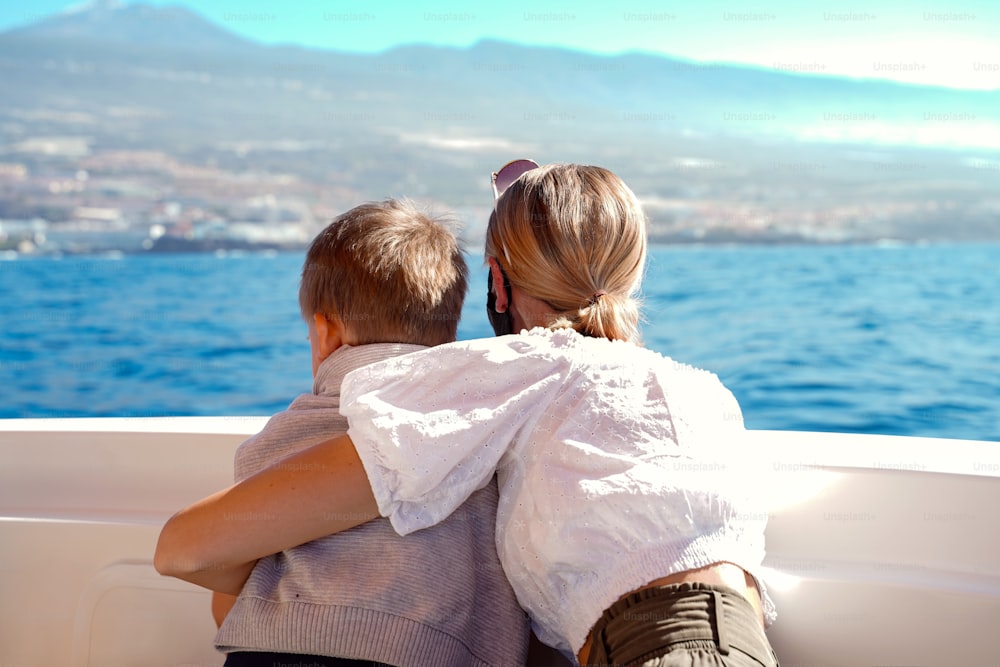 Happy traveler mother and little son enjoying island from deck of sailing boat, searching for dolphins. Summer vibes. Family lifestyle concept.