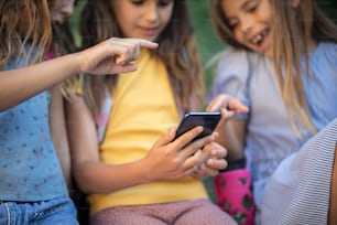 Trois petites filles utilisant un téléphone intelligent dans la nature. Concentrez-vous sur les mains.