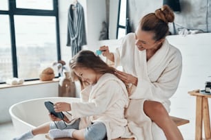 Beautiful young mother combining her daughter's hair while doing morning routine